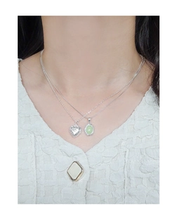 Detail of S925 silver embossed heart pendant and green gemstone necklace layering
