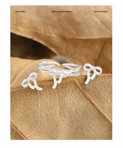 Detailansicht eines silbernen Schleifen-Schmucksets auf Trockenblättern mit Ring und Ohrsteckern