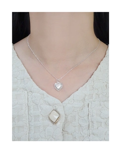 Detail view of a silver heart pendant with vintage embossed texture worn by a model