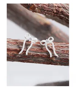 Detailed view of silver bow-shaped stud earrings with zircon on a rustic bark