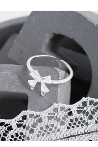 Detail of silver S925 bow-knot open ring on elegant white lace and grey geometric decor