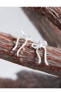 Detailed view of silver bow earrings with zircon stones on a rustic wood branch