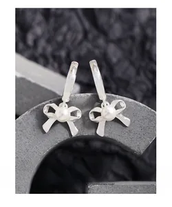 Macro detail of S925 silver bow earrings with round white pearl on a stone stand
