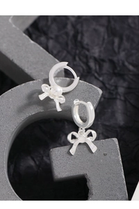 Close-up of S925 sterling silver bow earrings with white pearls on a grey stone base