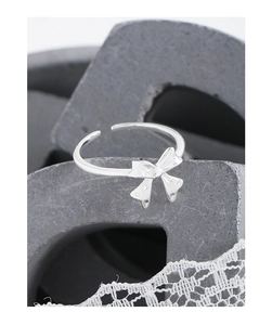 Detailed view of an adjustable silver bow ring with polished finish on a lace background