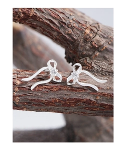 Macro shot of silver ribbon bow earrings with sparkling cubic zirconia on wood bark