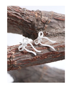 Detail of silver ribbon bow earrings with zircon on natural tree bark background