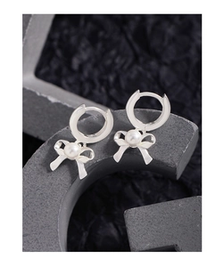 Detail of silver bow hoop earrings with center pearl on a decorative grey prop