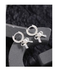 Macro detail of silver bow earrings with round white pearl inlays on a textured background