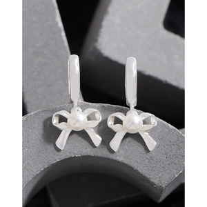 Elegant S925 silver bow earrings with round white pearls displayed on minimalist stone blocks