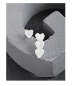 Macro view of asymmetrical silver heart stud earrings on a grey textured stand