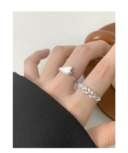 Detail of silver heart ring and woven chain band on finger for elegant styling