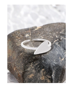 Close-up of minimalist silver heart-shaped open ring placed on textured natural stone