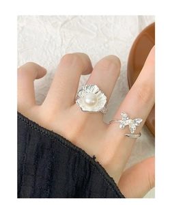Detail of silver S925 shell and butterfly pearl rings worn on a hand against texture