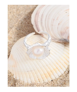 Macro view of shell-shaped S925 silver ring with pink pearl on beach background