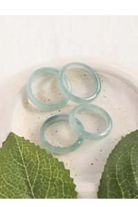 Close-up of four minimalist light green jade rings on a ceramic tray with green leaves