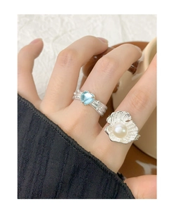 Close-up of shell-shaped silver ring with white pearl and heart-shaped blue gemstone ring