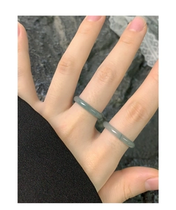 Detail of two slim minimalist green jadeite rings worn on fingers against rock background