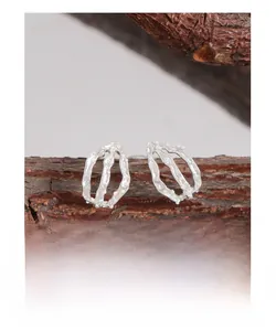 Detail of irregular texture silver earrings displayed on a natural branch texture