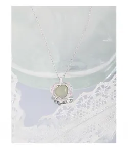 Vue macro du collier cœur en argent S925 avec opale verte sur verre et dentelle