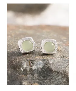 Detail of silver S925 earrings with hammered texture and green crystal on a natural rock