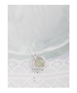 Gros plan du collier coeur en argent S925 avec cristal vert sur fond de dentelle élégant