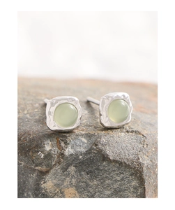 Macro view of light green crystal stud earrings with hammered texture on a rock