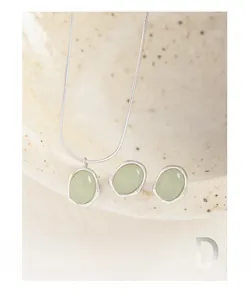 Detail view of silver necklace and green stone earrings set on a ceramic dish