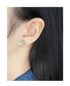 Close-up of minimalist light green oval crystal stud earring with silver setting on ear