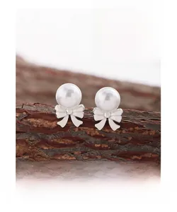 Macro detail of S925 silver bow stud earrings with white pearl on wooden branch