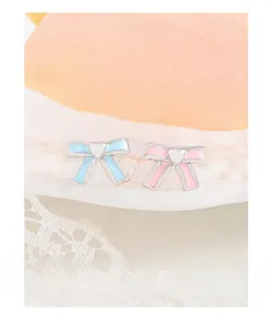 Macro detail of asymmetric pink and blue enamel bow earrings with white heart centers