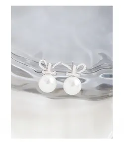 Close-up of S925 silver bow stud earrings with elegant white pearls on glass background