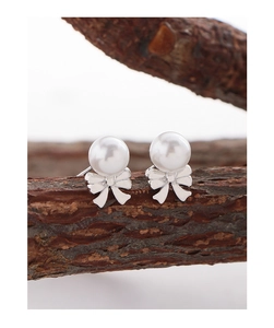 Detail of S925 silver bow stud earrings with white pearls on a natural wood branch