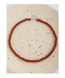 Close-up of S925 sterling silver lobster clasp and red agate beads on a ceramic plate