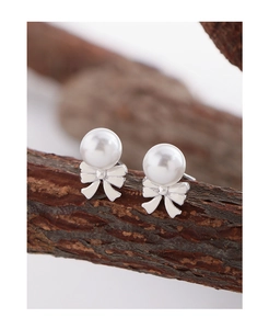Close-up of elegant pearl and silver bow stud earrings resting on a natural branch