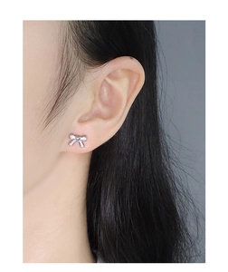 Close-up of S925 silver bow earrings with pink enamel on female model's ear