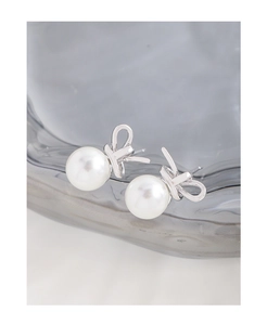 Detailed close-up of S925 silver bow stud earrings with round white pearls on a glass tray
