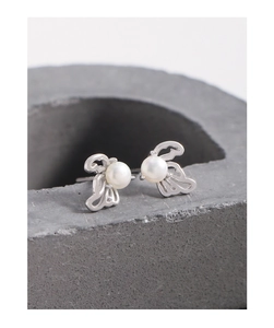 Macro shot of silver hollow wing earrings with white round pearls on grey stone