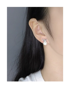 Detail of S925 silver bow stud earring with round white pearl on a model ear