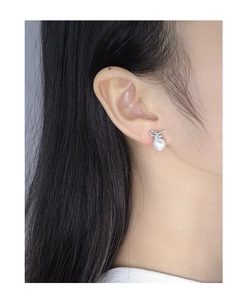 Close-up of S925 silver bow and pearl earrings worn by a model for a refined look