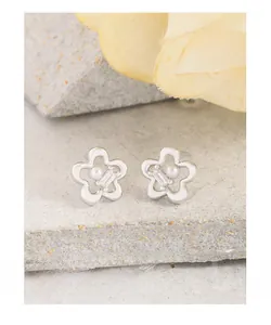Detailed view of silver flower earrings with zircon stones and pearls on stone base