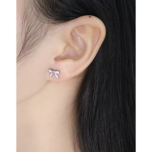 Minimalist S925 sterling silver bow earrings with pink enamel on a female model's ear