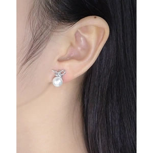 Elegant S925 silver bow stud earrings with white pearls shown on a female model