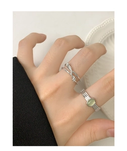 Close-up of S925 sterling silver knotted ring and light green gemstone ring on finger