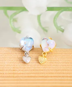 Macro detail of S925 silver heart stud earrings with iridescent moonstone and gold accents