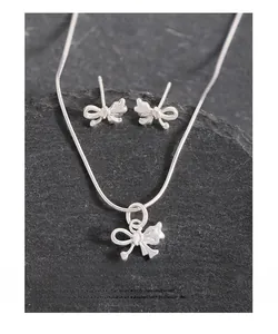 Macro detail of asymmetric silver bow earrings and necklace on dark textured stone