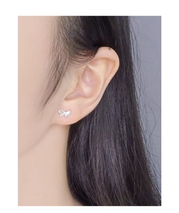Close-up detail of a delicate S925 silver asymmetric bow earring worn on a model ear