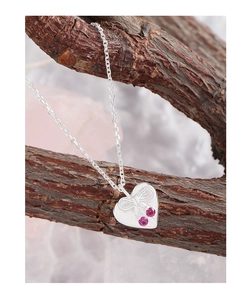 Macro view of bow-engraved heart pendant with pink zircon hung on a branch