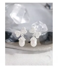 Detail of silver bow earrings with natural drop pearls and hammered texture on white background