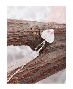 Macro shot of silver bow heart pendant with pink crystals on rustic wood branch